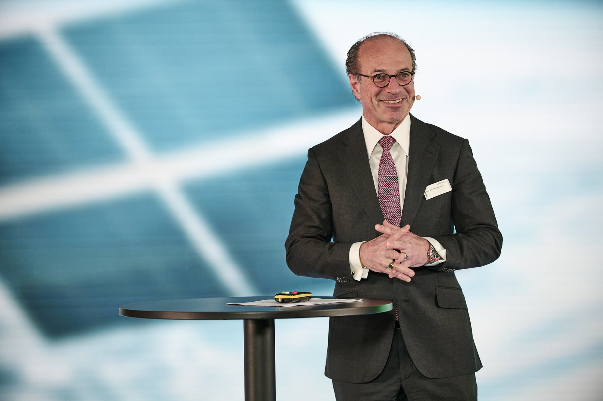 Ulrich Hermann smiling at a standing table in front of a projection showing satellite solar panels.