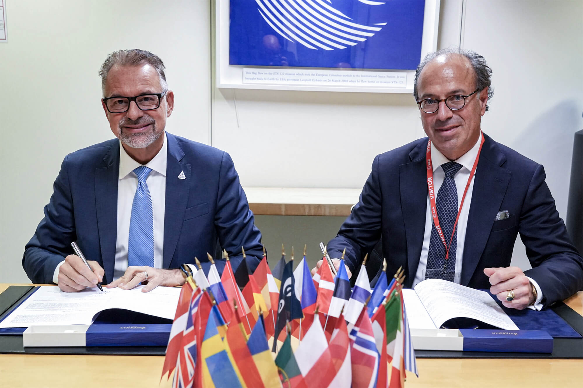 Unterzeichnung einer Partnerschaftsvereinbarung mit der ESA vor internationalen Flaggen durch Ulrich Hermann und Josef Ascherbacher