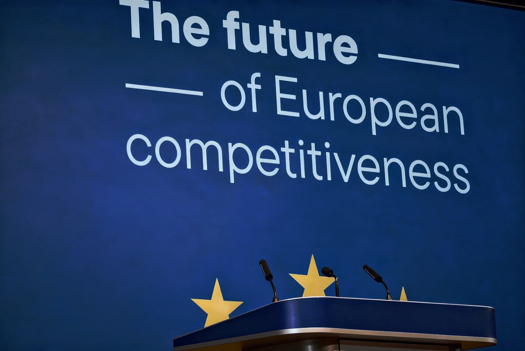 EU institutional podium with golden stars and microphones, large screen in background reading "The future of European competitiveness".
