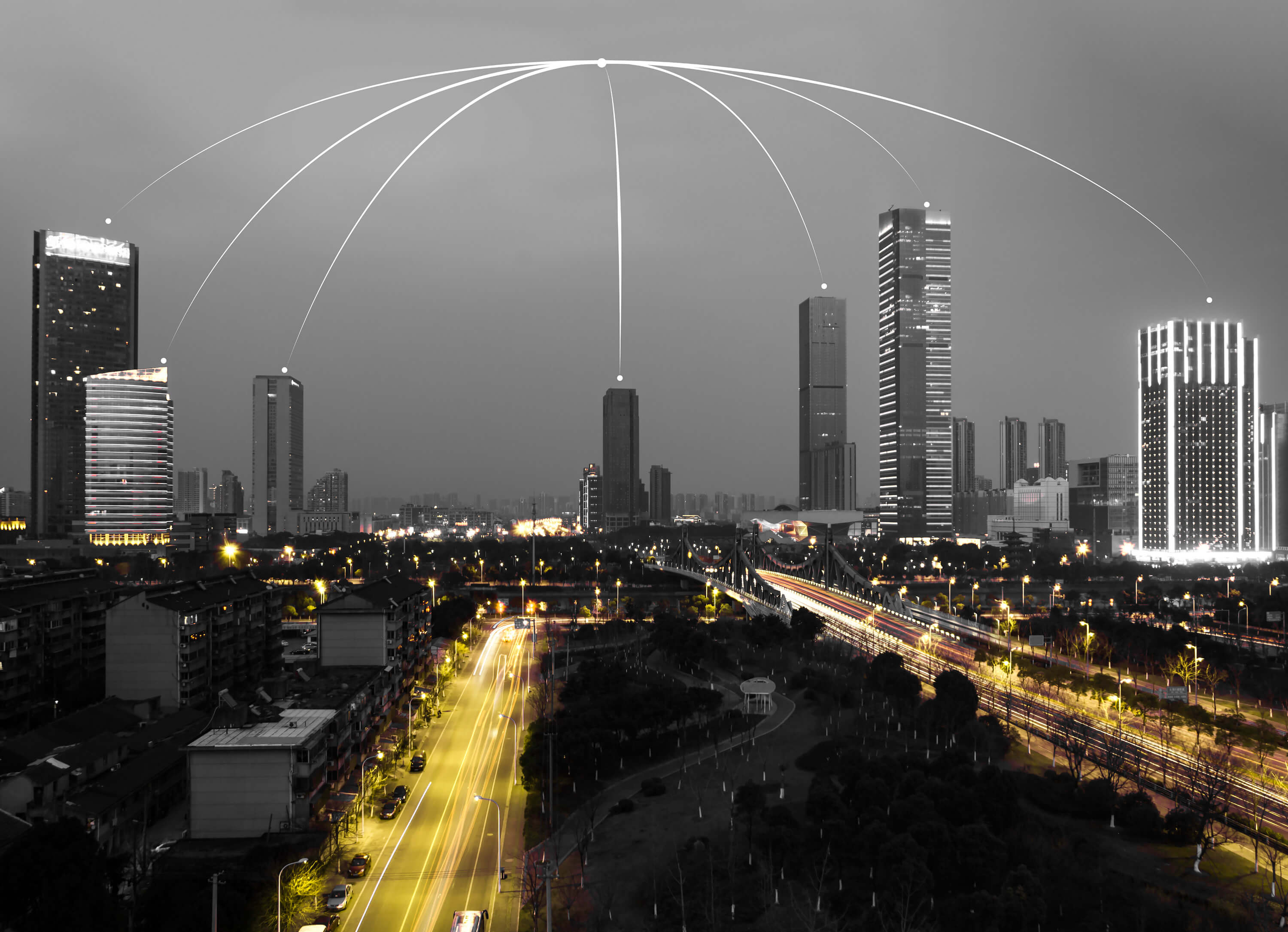 Black and white night cityscape with illuminated highways and skyscrapers, overlaid with white arc lines connecting nodes across the skyline to symbolize infrastructure networks.